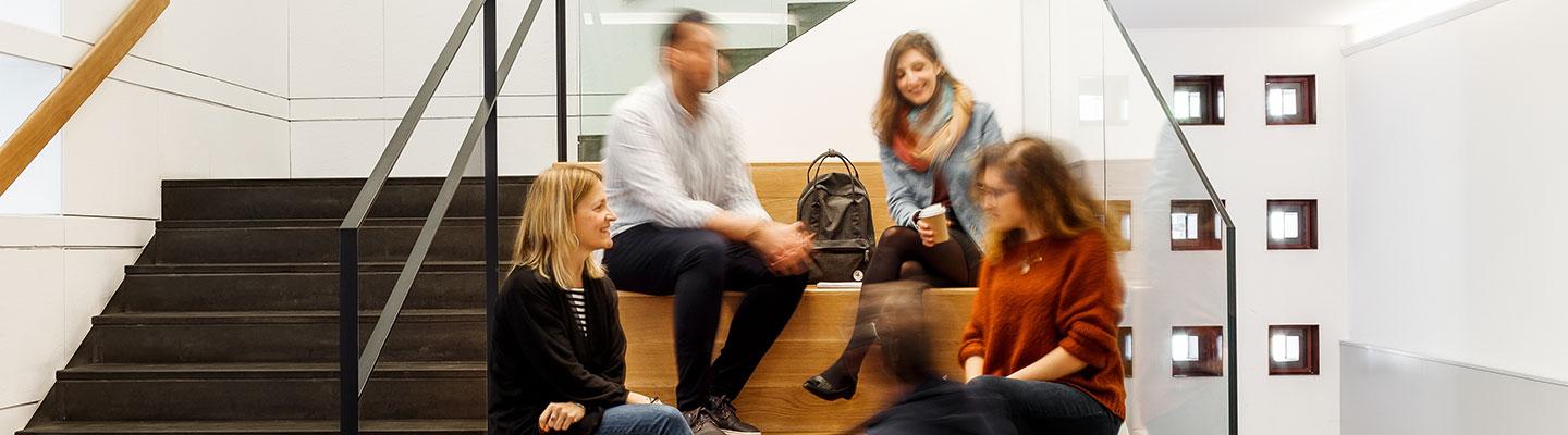 Group of students chatting on wooden steps in a bright, modern campus stairwell