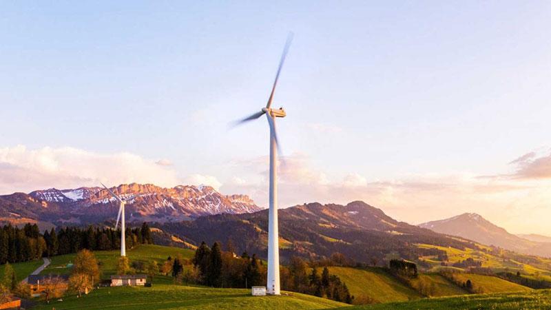 Wind turbines in a green valley at sunset, with mountains in the background.