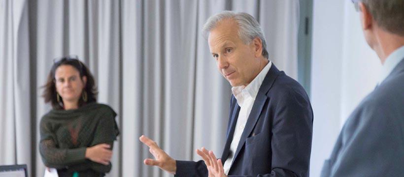 Professor presenting to students, gesturing in a classroom.