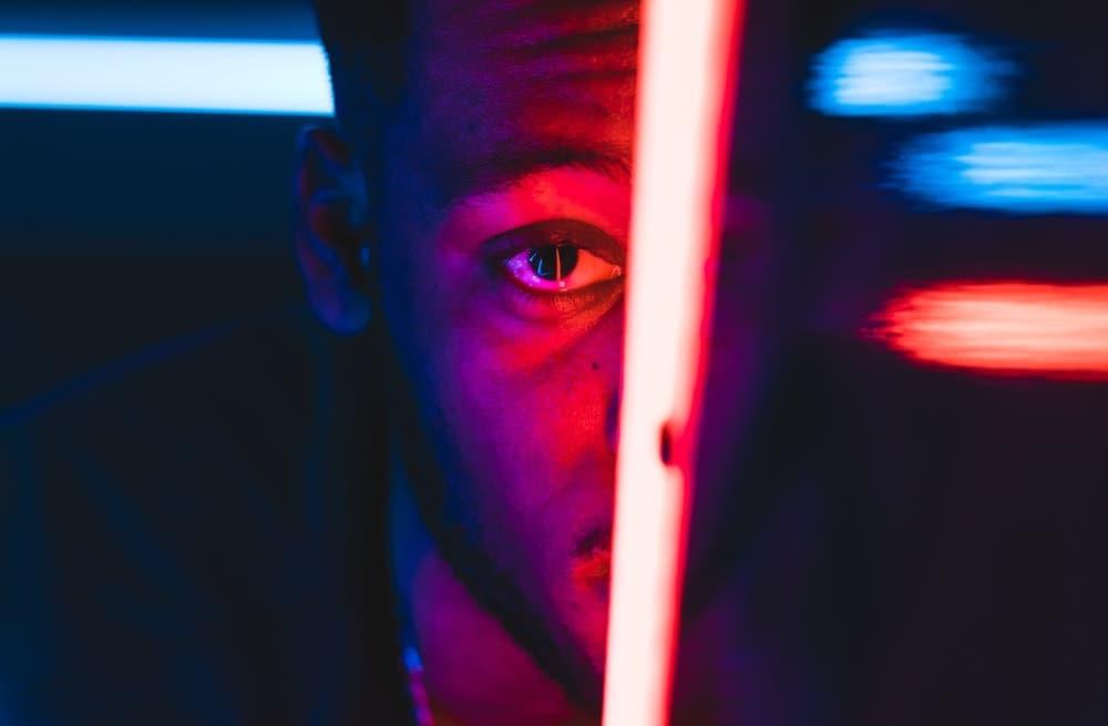 Un hombre mira de frente a traves de un panel de luces de neón