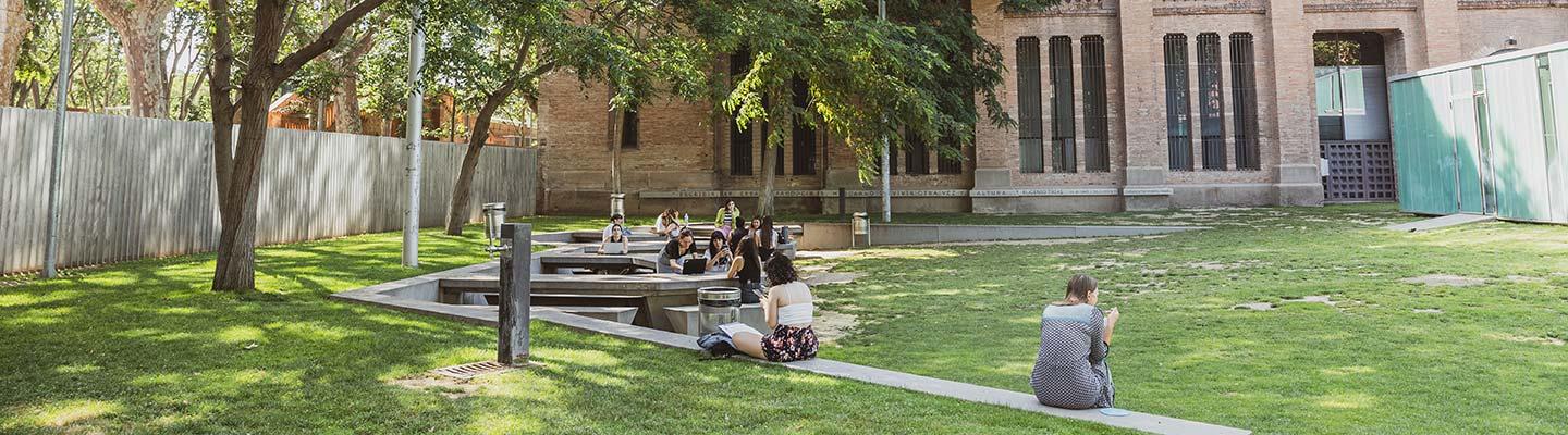 Students studying and relaxing on a green campus lawn beside a historic brick building.