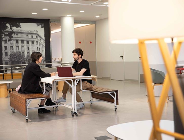 Two students working together on a laptop in a modern common area at UPF Barcelona School of Management.