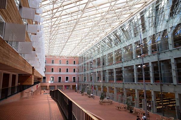 UPF atrium with glass walls, red brick flooring, and natural light from a geometric glass ceiling.